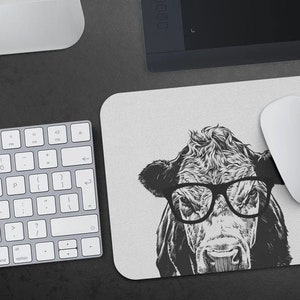 May include: A black and white illustration of a cow wearing glasses on a white mouse pad. The cow is looking directly at the viewer.