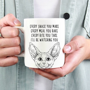 May include: White ceramic mug with a black and white illustration of a cat with the text "EVERY SNACK YOU MAKE EVERY MEAL YOU BAKE EVERY BITE YOU TAKE I'LL BE WATCHING YOU"