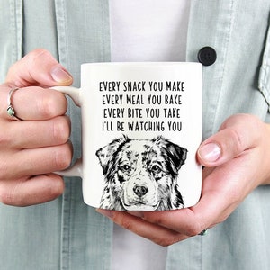 Peut inclure: Une tasse en céramique blanche avec une illustration en noir et blanc d'un Berger australien. La tasse porte le texte "Every snack you make, every meal you bake, every bite you take, I'll be watching you."