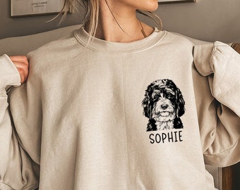May include: A beige sweatshirt with a black and white illustration of a dog's head and the name "Sophie" printed on the front.