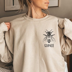 May include: A beige sweatshirt with a black bee graphic and the name "Sophie" printed below it.