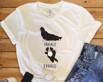 May include: White t-shirt with a graphic of a Bernese Mountain Dog doing yoga poses. The text "inhale" and "exhale" are printed below the dog images.