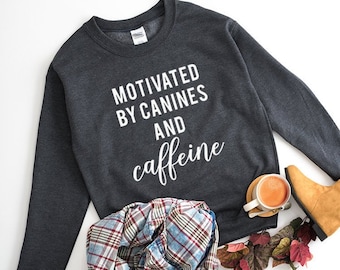 May include: A dark gray sweatshirt with the text "Motivated by Canines and Caffeine" in white lettering.