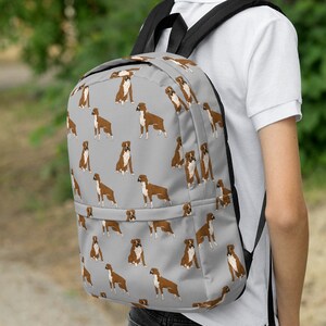 May include: A gray backpack with a repeating pattern of brown boxer dogs. The backpack has black straps and a black zipper.