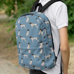 May include: A blue backpack with a pattern of brown and white German Shorthaired Pointers. The backpack has black straps and a black zipper.