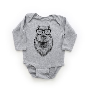 Puede incluir: Un body de bebé gris de manga larga con una ilustración en blanco y negro de un capibara con gafas.