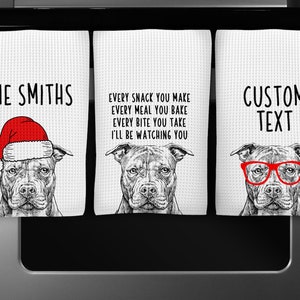 May include: Three kitchen towels with a black and white illustration of a Pit Bull dog. The first towel has the text "THE SMITHS" and the dog is wearing a red Santa hat. The second towel has the text "EVERY SNACK YOU MAKE EVERY MEAL YOU BAKE EVERY BITE YOU TAKE I'LL BE WATCHING YOU". The third towel has the text "CUSTOM TEXT" and the dog is wearing red glasses.