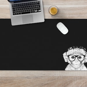 May include: Black desk mat with a white illustration of a monkey wearing glasses. The monkey is looking at the viewer.