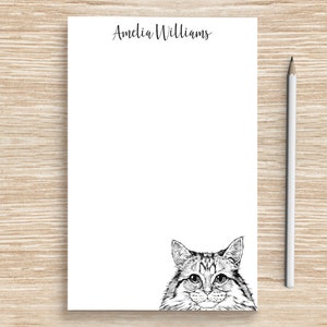 May include: White notepad with black ink, featuring the name "Amelia Williams" at the top and a black and white illustration of a cat's face peeking from the bottom.