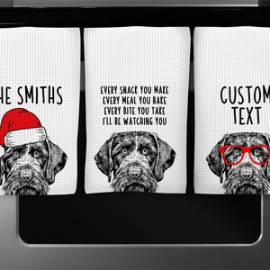 May include: Three kitchen towels with a black and white illustration of a dog wearing a Santa hat, glasses, and a plain design. The text on the towels reads "THE SMITHS", "EVERY SNACK YOU MAKE EVERY MEAL YOU BAKE EVERY BITE YOU TAKE I'LL BE WATCHING YOU", and "CUSTOM TEXT".
