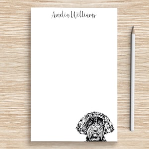 K&ouml;nnte beinhalten: Wei&szlig;er Notizblock mit schwarzer Tinte, der Name "Amelia Williams" oben und eine Schwarzwei&szlig;illustration eines Hundekopfes, der unten herausguckt.