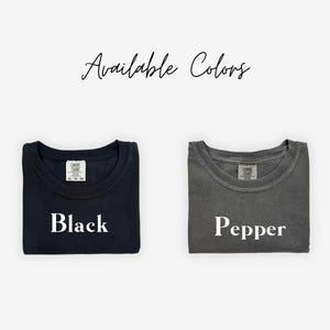 May include: Two folded t-shirts, one black and one pepper-colored, are displayed against a white background. The text "Available Colors" is written in cursive at the top. The black shirt has the word "Black" printed on it, and the pepper shirt has the word "Pepper".