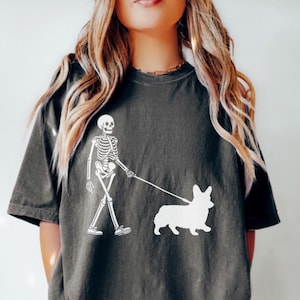 May include: A dark gray t-shirt with a white graphic of a skeleton walking a corgi.