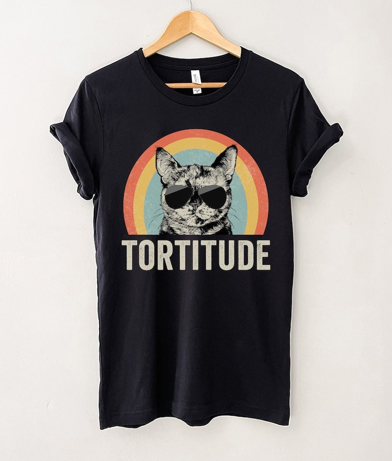 May include: Black t-shirt with a retro rainbow design and a cat wearing sunglasses. The text "TORTITUDE" is printed below the cat.