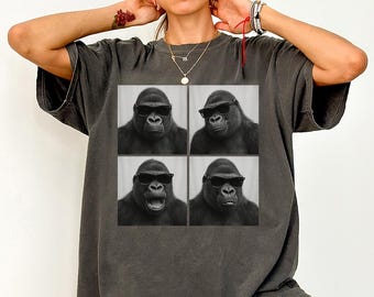 May include: Dark gray t-shirt featuring a black and white graphic of a gorilla wearing sunglasses in four different poses. The shirt is a relaxed fit and has short sleeves.