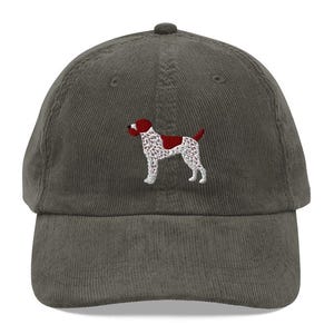 Peut inclure: Casquette de baseball en velours côtelé vert. Elle présente une broderie d'un chien avec des marques rouges et blanches. Le chien est debout, la queue et la tête relevées. Style classique.