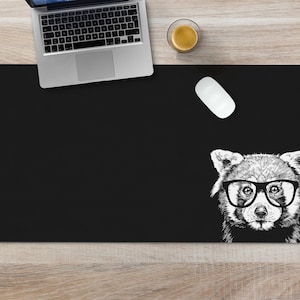 May include: Black desk mat with a white illustration of a red panda wearing glasses. The red panda is looking directly at the viewer.