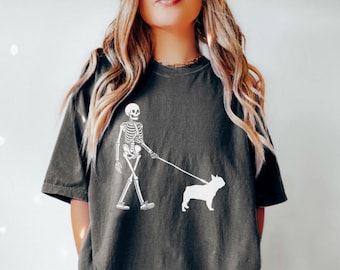 May include: A dark gray t-shirt with a white graphic of a skeleton walking a french bulldog.