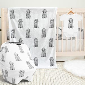 May include: A nursery set featuring a white blanket, car seat cover, and onesie, all adorned with a repeating black and white illustration of a puppy. The onesie is hanging on a wooden hanger. A crib is in the background.