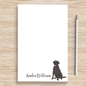 May include: A white notepad with a black Labrador Retriever illustration and the name "Amelia Williams" written in black cursive.
