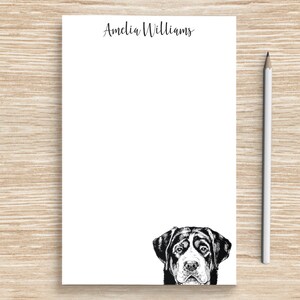 May include: A white notepad with the name "Amelia Williams" printed at the top. The notepad has a black and white illustration of a dog's head peeking out from the bottom.