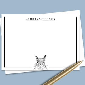 May include: White stationery with a black border and the name "AMELIA WILLIAMS" at the top. A detailed black and white illustration of a squirrel is at the bottom. A gold pen rests on the stationery.