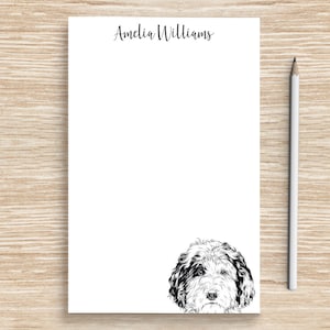 May include: A white notepad with the name "Amelia Williams" printed at the top. A black and white illustration of a dog's head is at the bottom of the notepad.