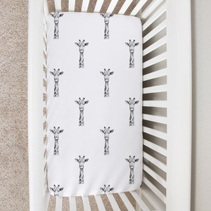 May include: White crib with a white fitted sheet featuring a black and white giraffe print. The sheet has a repeating pattern of giraffe heads.