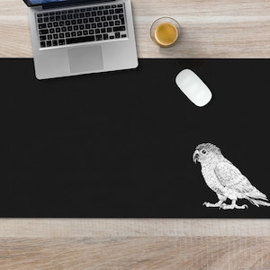 May include: Black desk mat with a white illustration of a parrot on the right side. A white computer mouse is on the mat.