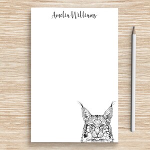 May include: A white notepad with the name "Amelia Williams" printed at the top. The notepad has a black and white illustration of a lynx's face at the bottom.