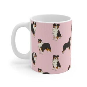 May include: White ceramic mug with a pink background and a repeating pattern of black and brown Australian Shepherd dogs.
