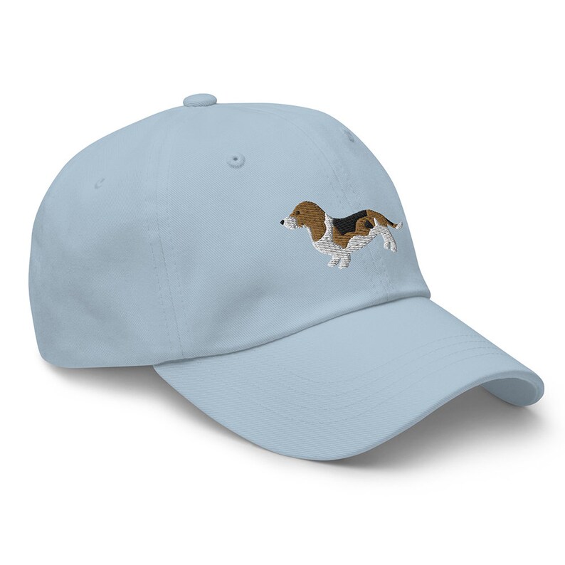 A light blue baseball cap with an embroidered brown and white basset hound on the front.