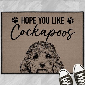 May include: Tan doormat with a black border featuring the text "HOPE YOU LIKE Cockapoos" and paw prints. A Cockapoo dog illustration is at the bottom. Black canvas sneakers are at the bottom of the image.