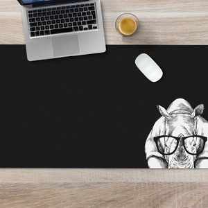 May include: Black desk mat with a white illustration of a rhinoceros wearing glasses. The rhinoceros is looking directly at the viewer.