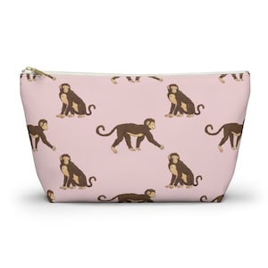 May include: A pink zippered pouch with a repeating pattern of brown monkeys. The monkeys are in various poses, some sitting and some walking.