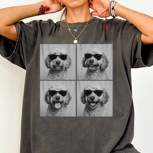 May include: Dark grey t-shirt with a square graphic showing a dog wearing sunglasses in four poses. The dog has curly fur and is smiling in two of the images. The shirt has a relaxed fit.