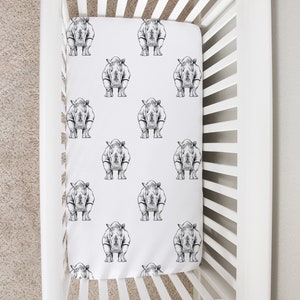 May include: White crib with a white fitted sheet featuring a black and white rhino print. The sheet has a repeating pattern of rhinos.