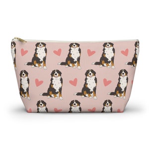 May include: Pink zippered makeup bag with a repeating pattern of Bernese Mountain Dogs and pink hearts.