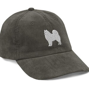 May include: A dark green corduroy baseball cap with a white embroidered image of a Samoyed dog.
