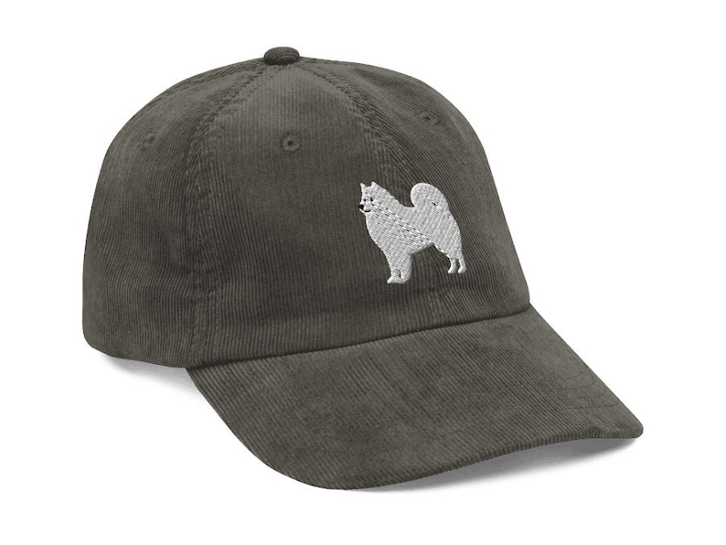 May include: A dark green corduroy baseball cap with a white embroidered image of a Samoyed dog.