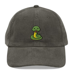 May include: A dark grey corduroy baseball cap with an embroidered cartoon snake. The snake has a green body, yellow belly, and a red tongue. The cap has a curved peak and a fabric strap closure.