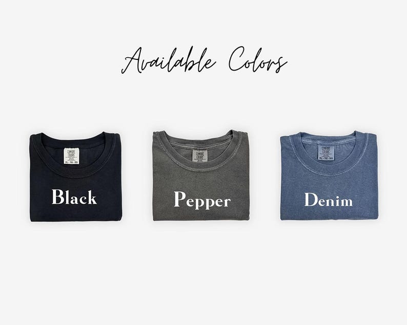 May include: Three folded t-shirts in different colors: black, pepper, and denim. The shirts are laid out on a white background with the word "Available Colors" written above them.
