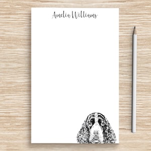 May include: A white notepad with the name "Amelia Williams" printed at the top. A black and white illustration of a Springer Spaniel dog's head is at the bottom of the notepad.