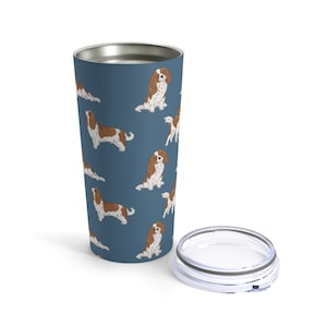 May include: A stainless steel tumbler with a blue background and a repeating pattern of Cavalier King Charles Spaniel dogs. The tumbler has a clear lid.