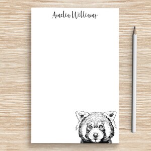May include: A white notepad with the name "Amelia Williams" printed at the top. The notepad has a black and white illustration of a red panda peeking out from the bottom.