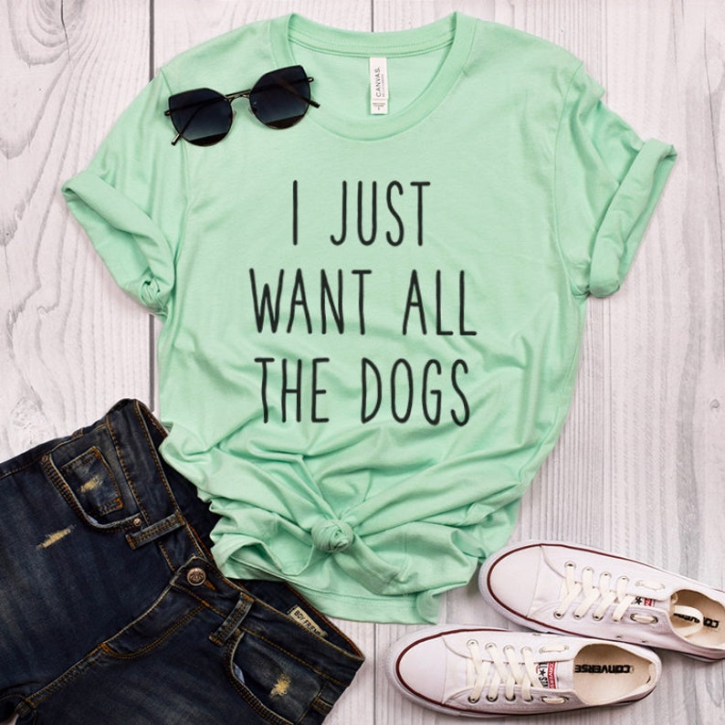 K&ouml;nnte beinhalten: Ein hellgr&uuml;nes T-Shirt mit dem Aufdruck "I just want all the dogs" in Schwarz. Das Shirt wird mit einer blauen Jeans und wei&szlig;en Turnschuhen kombiniert.