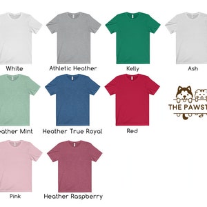 K&ouml;nnte beinhalten: Eine Auswahl an T-Shirt-Farben, darunter Wei&szlig;, Heather Grey, Kelly Gr&uuml;n, Asche, Heather Mint, Heather True Royal, Rot, Pink und Heather Raspberry. Alle T-Shirts sind kurz&auml;rmelig und haben einen Rundhalsausschnitt. Das Bild zeigt auch ein Logo mit dem Text "THE PAWSTER" und ein Cartoon-Bild eines Huskys und einer Katze.
