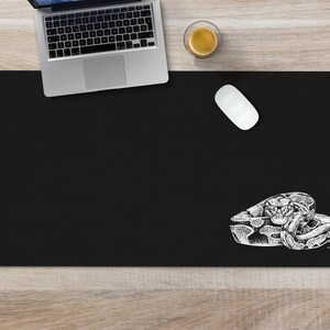 May include: Black desk mat with a white illustration of a snake curled up on the bottom right corner.