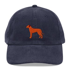 May include: A navy blue corduroy baseball cap with an orange embroidered dog silhouette.
