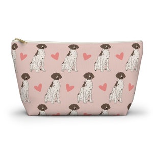 May include: A pink zippered pouch with a repeating pattern of brown and white German Shorthaired Pointers and pink hearts.